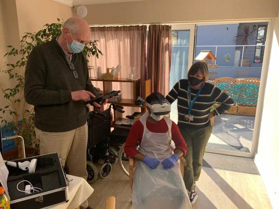 two medical professionals with a seated patient who is wearing a VR headset