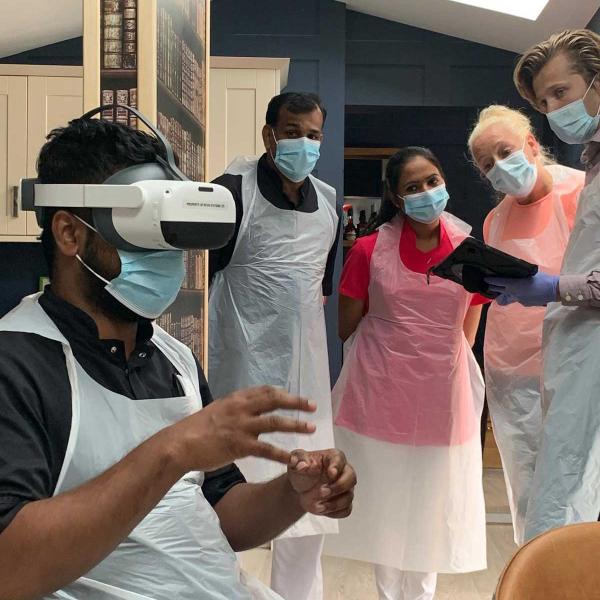 A group of medical professionals around a seated colleague who is wearing a VR headset