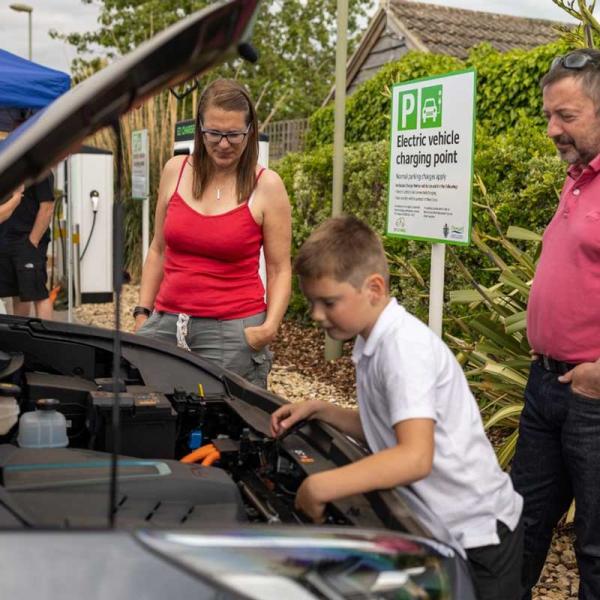 two adults and a child looking into the engine of an electric car