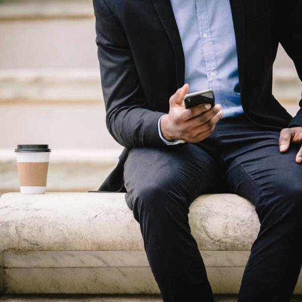 a man wearing a suit sitting on a wall looking at a mobile phone